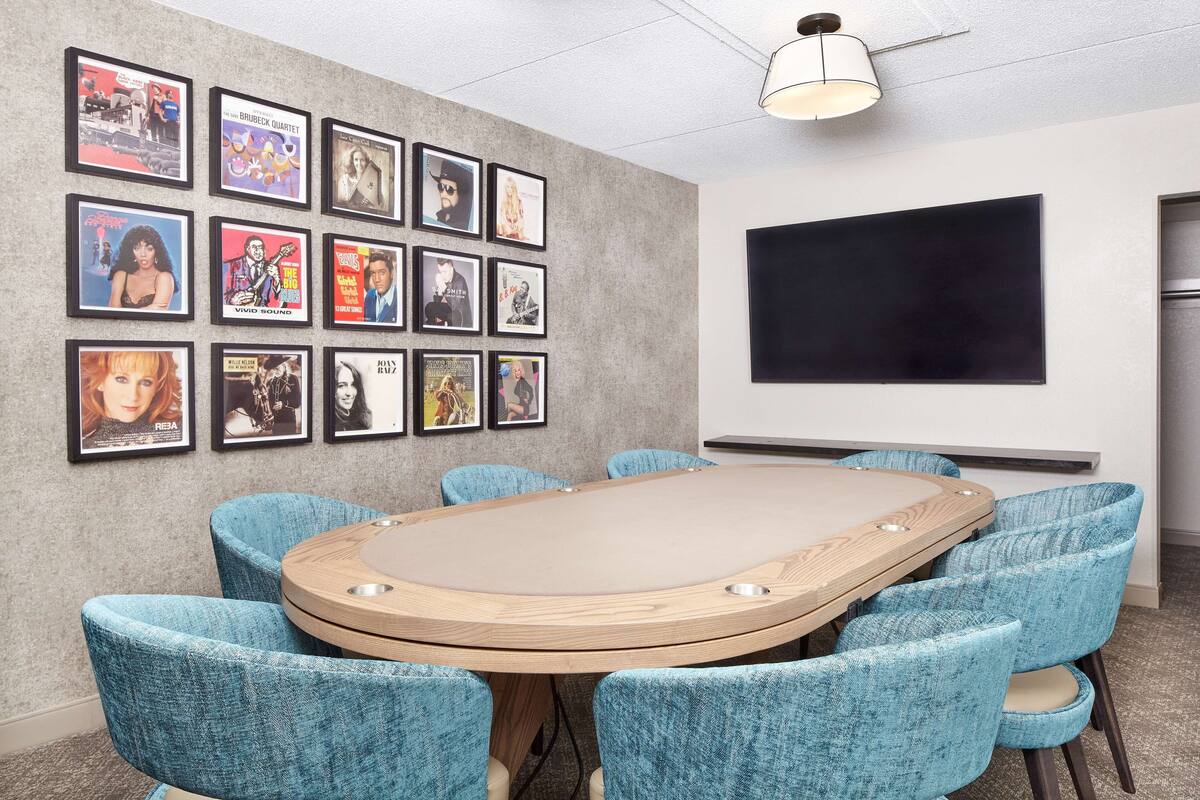 Een vergaderzaal met een ronde tafel, zes blauwe fauteuils en een muur versierd met ingelijste posters.