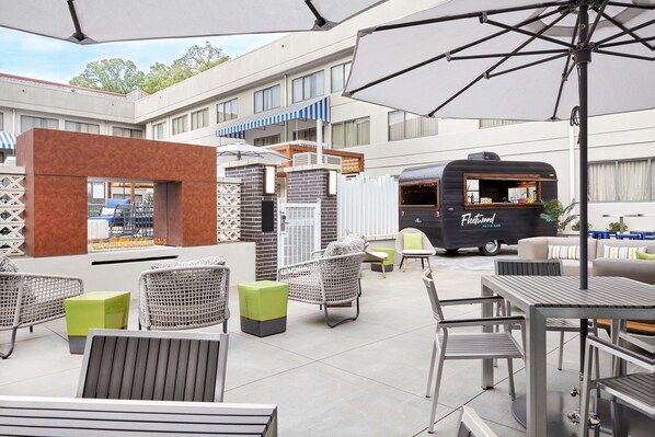 Un patio al aire libre con sillas de mimbre, una mesa y un camión de comida identificado como "Fleetwood Patio Bar".