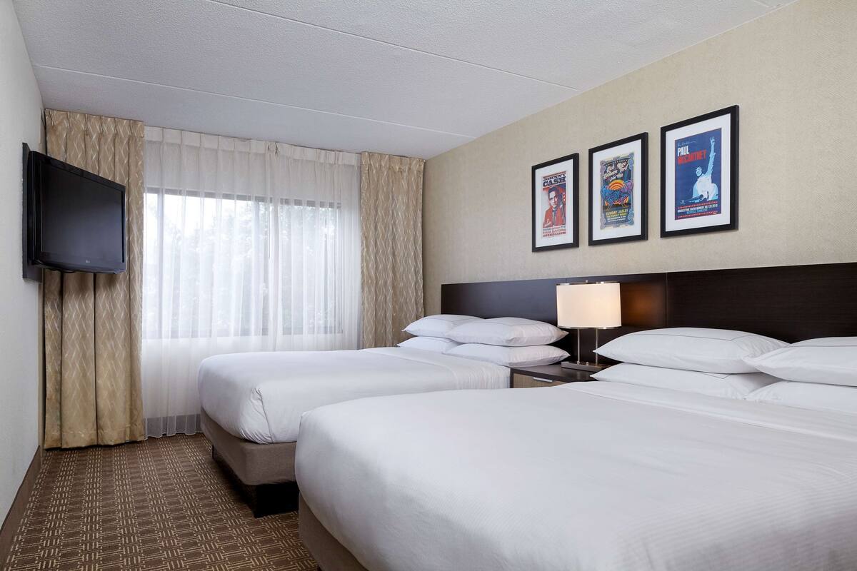 Een hotelkamer met twee bedden, een aan de muur bevestigde televisie en drie ingelijste posters.
