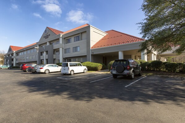 Un hotel con un estacionamiento y varios coches aparcados en la entrada.