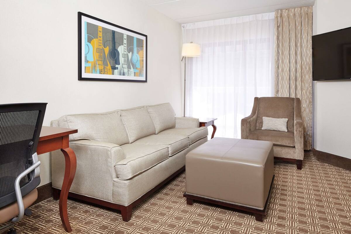 Een hotelkamer met een bank, een voetenbankje, een bureau met stoel, een televisie en een kamerbreed tapijt met dessin.