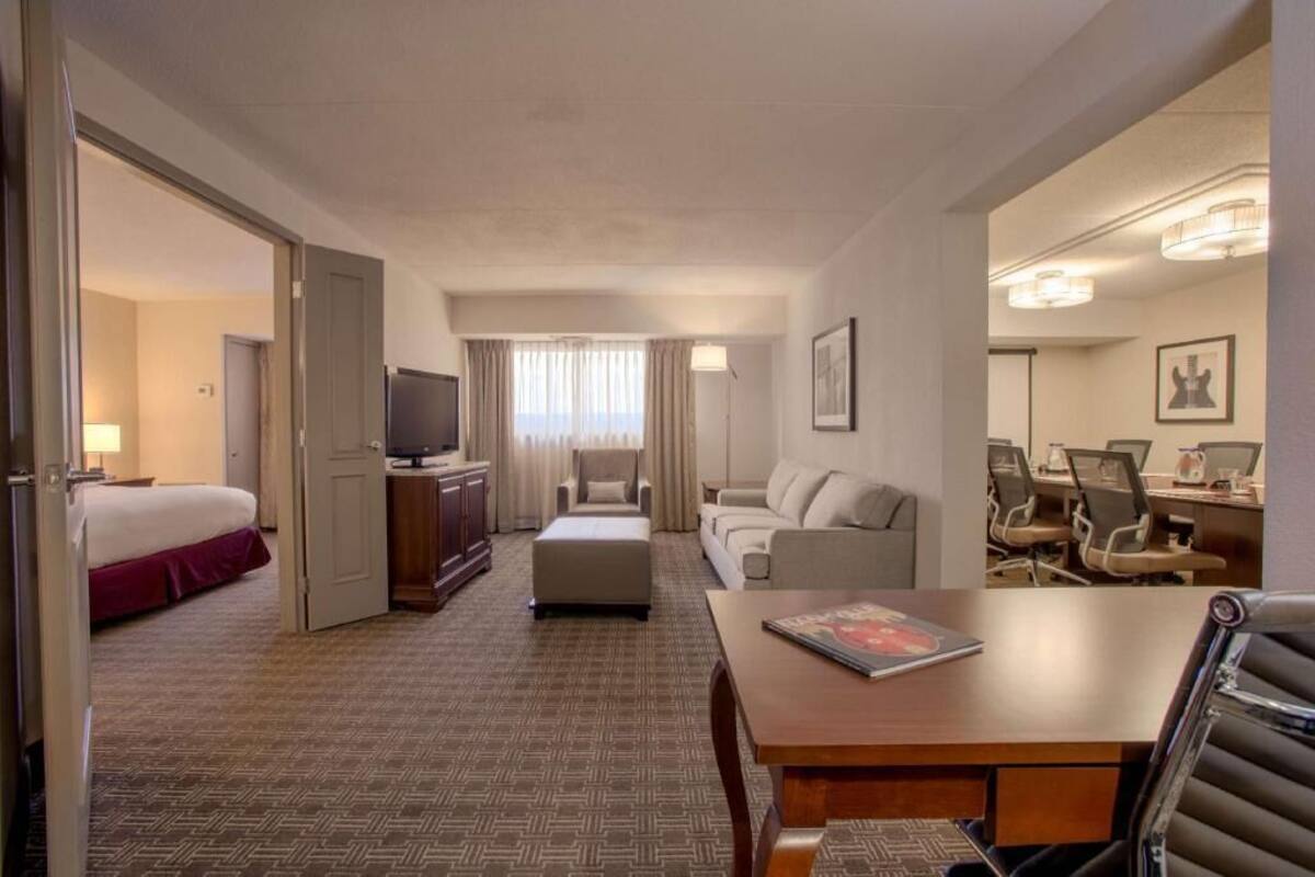 Ein Hotelzimmer mit Bett, Sofa, Esstisch, Fernseher und Schreibtisch mit Stühlen.