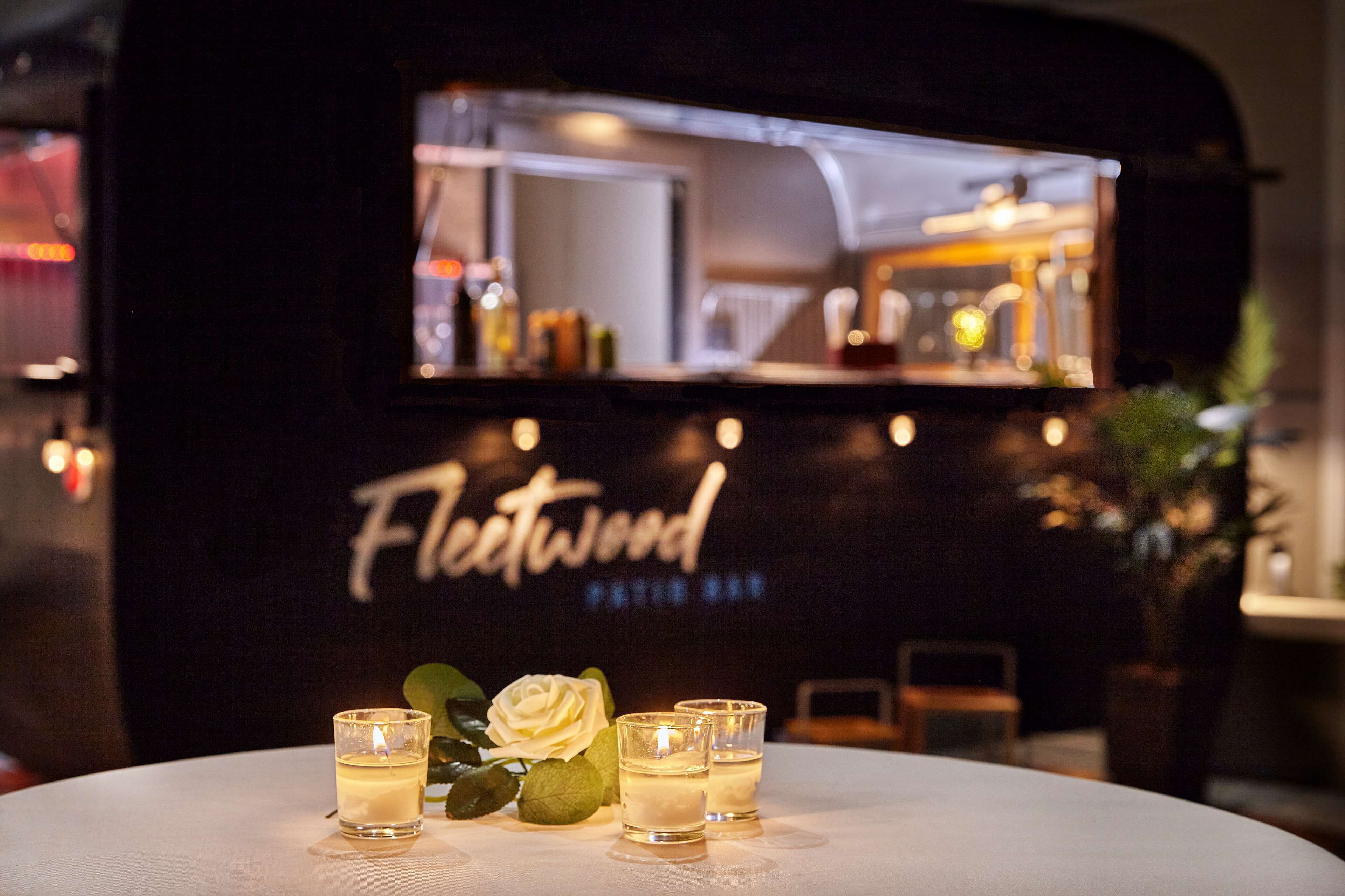 A bar area with a sign reading "Fleetwood" and three shot glasses on a table with a candle and a white rose.