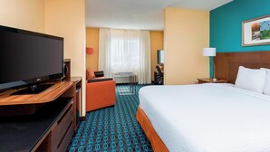 A hotel room with a large bed, a TV on a wooden stand, a desk with a chair, and a small table with a lamp. - Fairfield Inn & Suites Lincoln (Lincoln)
