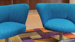 A reception area with two blue chairs, a colorful carpet, a map on the wall, and a framed certificate. - Fairfield Inn & Suites Lincoln (Lincoln)