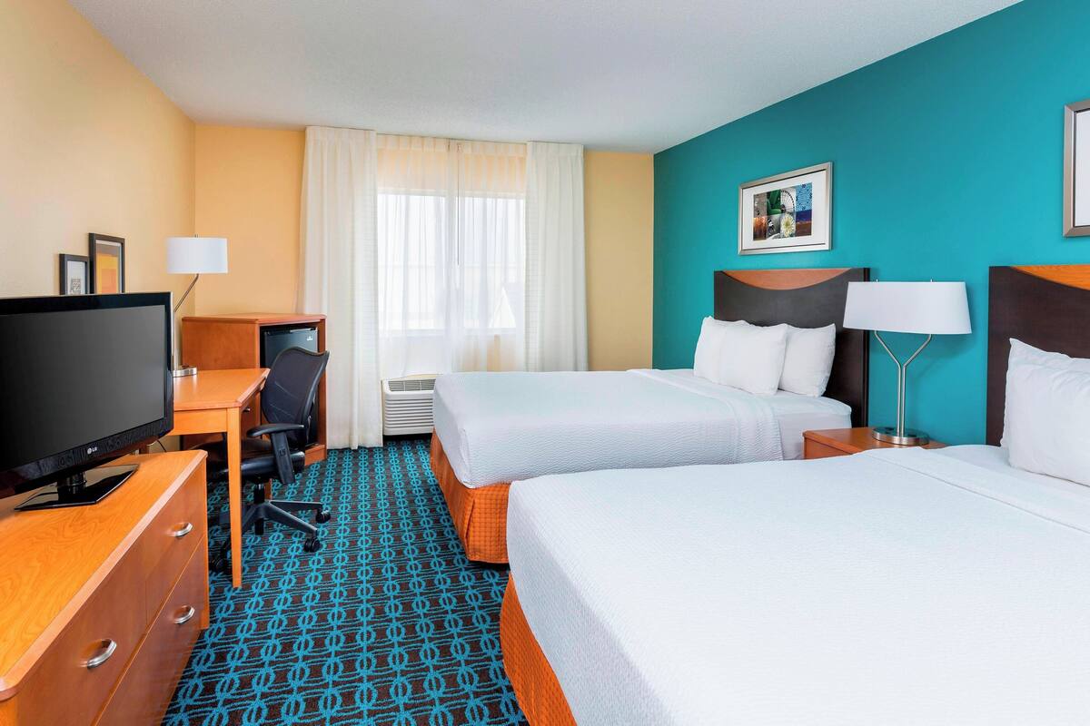 Een hotelkamer met twee bedden, een bureau met televisie en een raam met gordijnen.