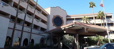 A multi-story hotel with a central courtyard, palm trees, and a flag.