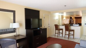 Une chambre d’hôtel équipée d’une télévision, d’un bureau, d’une chaise, d’un canapé et d’un coin cuisine.