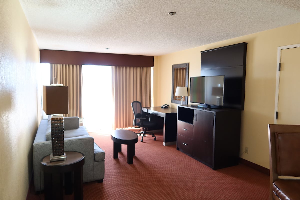 A hotel room with a sofa, a desk with a computer, a television, and a small table.
