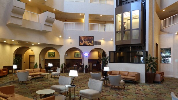 Un hall d’entrée spacieux, doté de plusieurs espaces de détente, d’un comptoir d’accueil central et d’une grande fenêtre donnant sur l’intérieur.