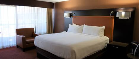 A hotel room with a large bed, a chair, a nightstand, and a water dispenser.