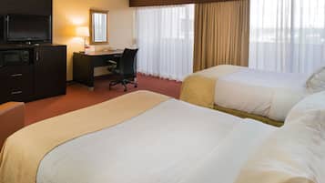 A hotel room with two beds, a desk, a television, and a window with curtains.