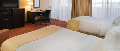 A hotel room with two beds, a desk, a television, and a window with curtains.