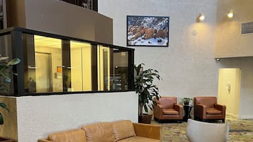 A lobby with a brown leather sofa, two armchairs, a coffee table, and a patterned carpet.