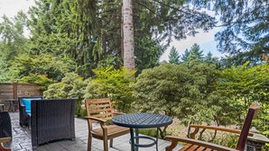 An outdoor patio with wicker furniture and a round table, surrounded by dense greenery and tall trees. - Best Western Plus Plaza by the Green (Kent)