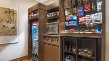 Une petite cuisine équipée d’un four à micro-ondes, d’un réfrigérateur et d’étagères remplies de collations et de condiments.