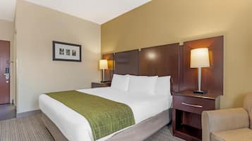 Quarto de hotel com uma cama grande, duas mesas de cabeceira com abajures, uma cadeira e um quadro na parede.