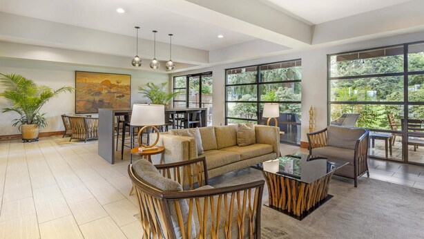 A spacious living area with a sofa, chairs, a coffee table, and a dining table. There are large windows with a view of greenery outside. - Best Western Plus Plaza by the Green (Kent)
