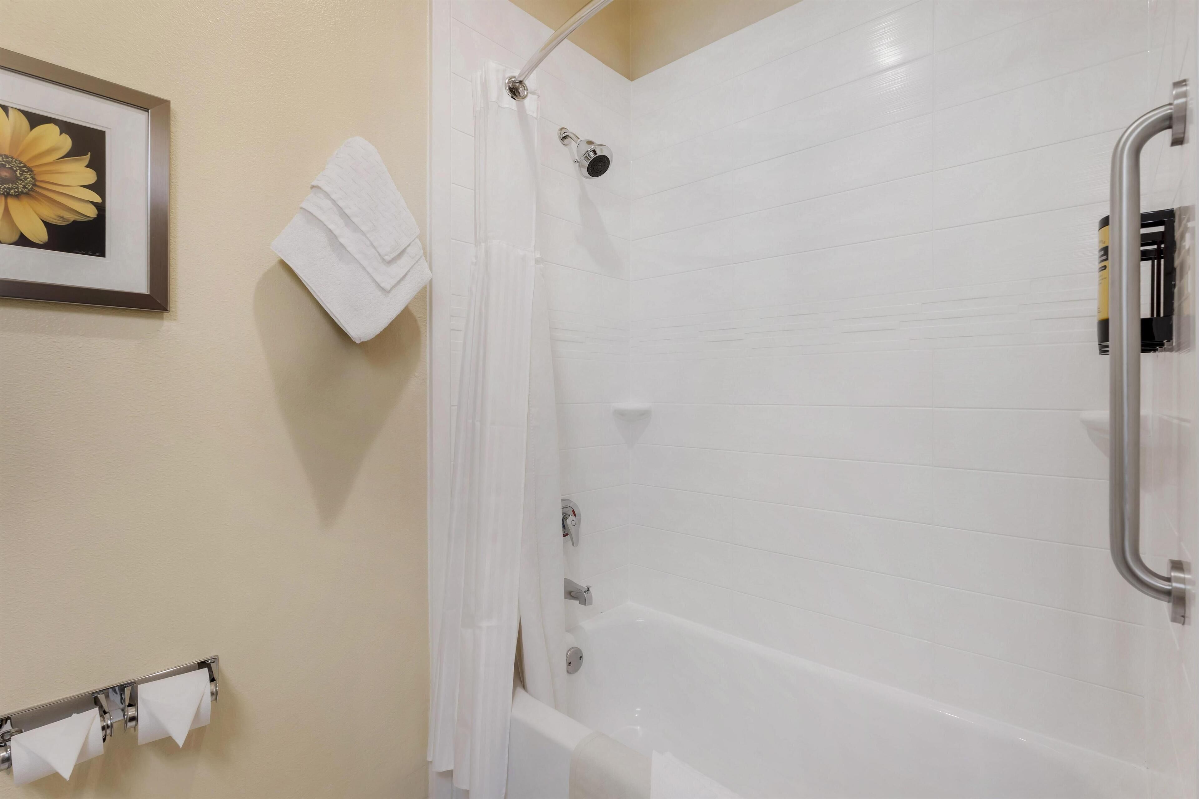 A bathroom with a shower, a framed flower on the wall, and a towel rack with towels.