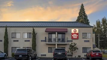 A Best Western Plus hotel with a parking lot, several SUVs parked, and a clear sky.