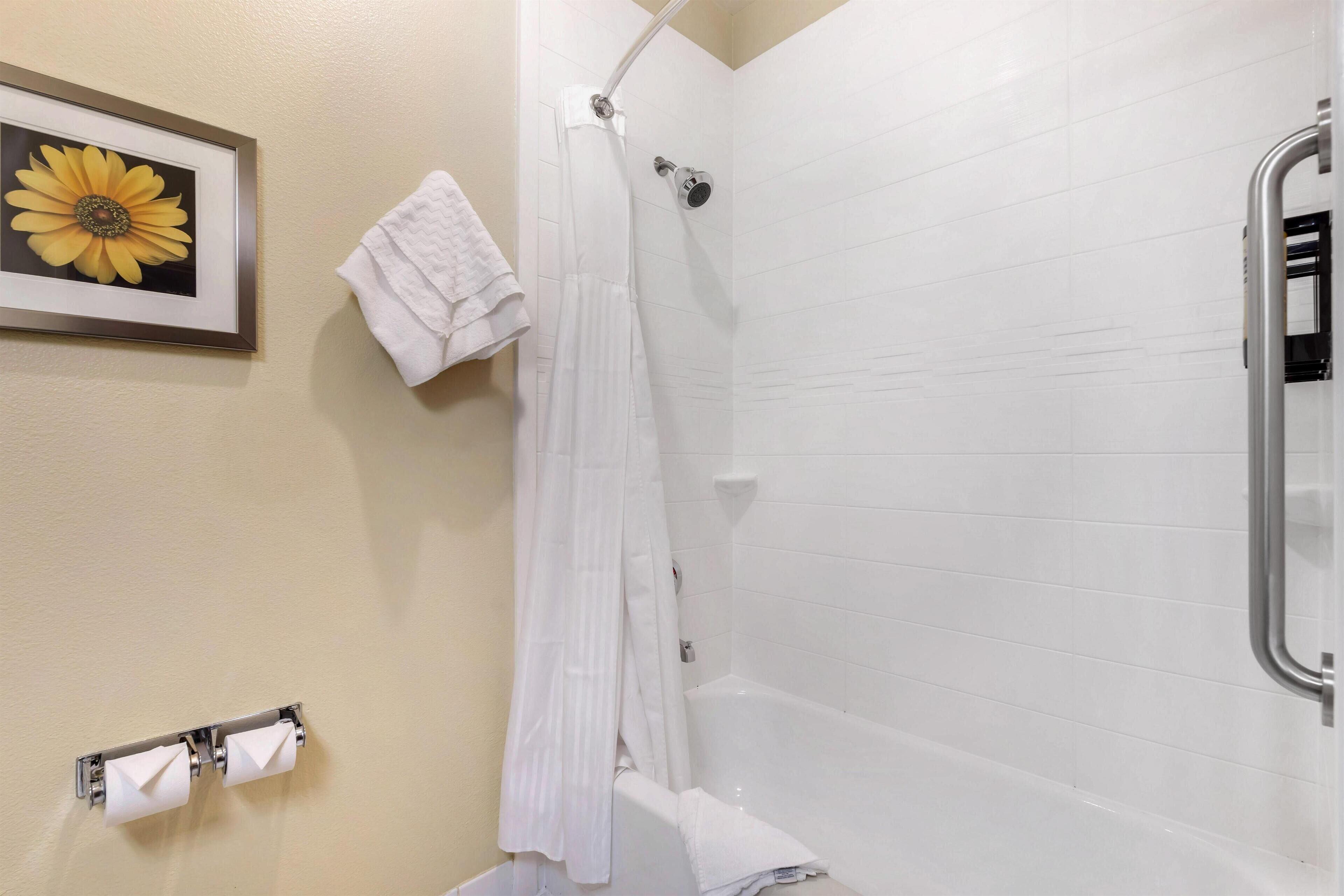 A bathroom with a shower, a framed flower on the wall, and a towel rack with towels.
