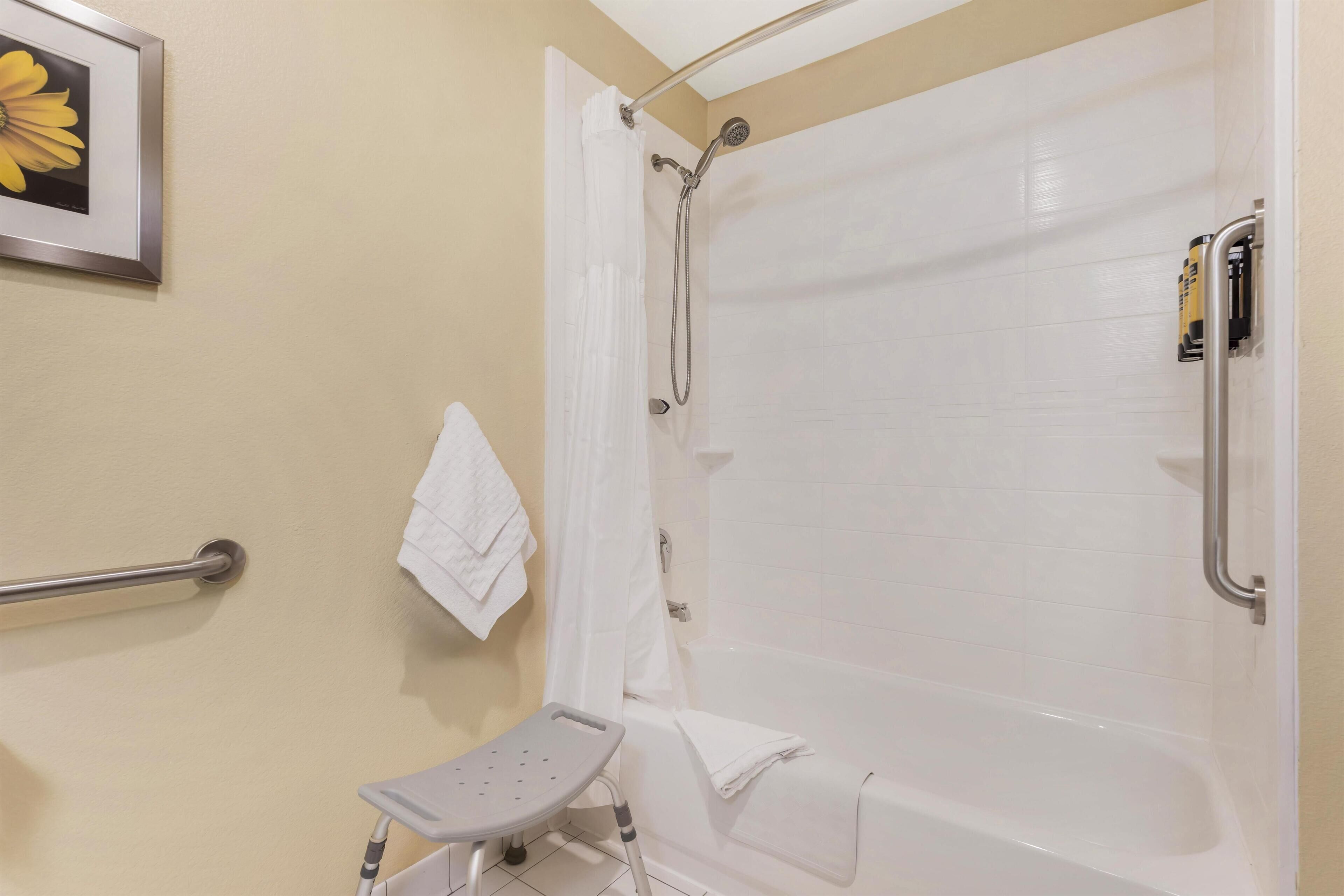 A bathroom with a shower, a grab bar, a white towel, and a framed picture on the wall.
