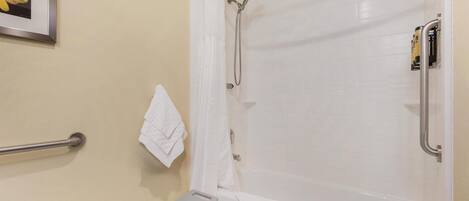 A bathroom with a shower, a grab bar, a white towel, and a framed picture on the wall.
