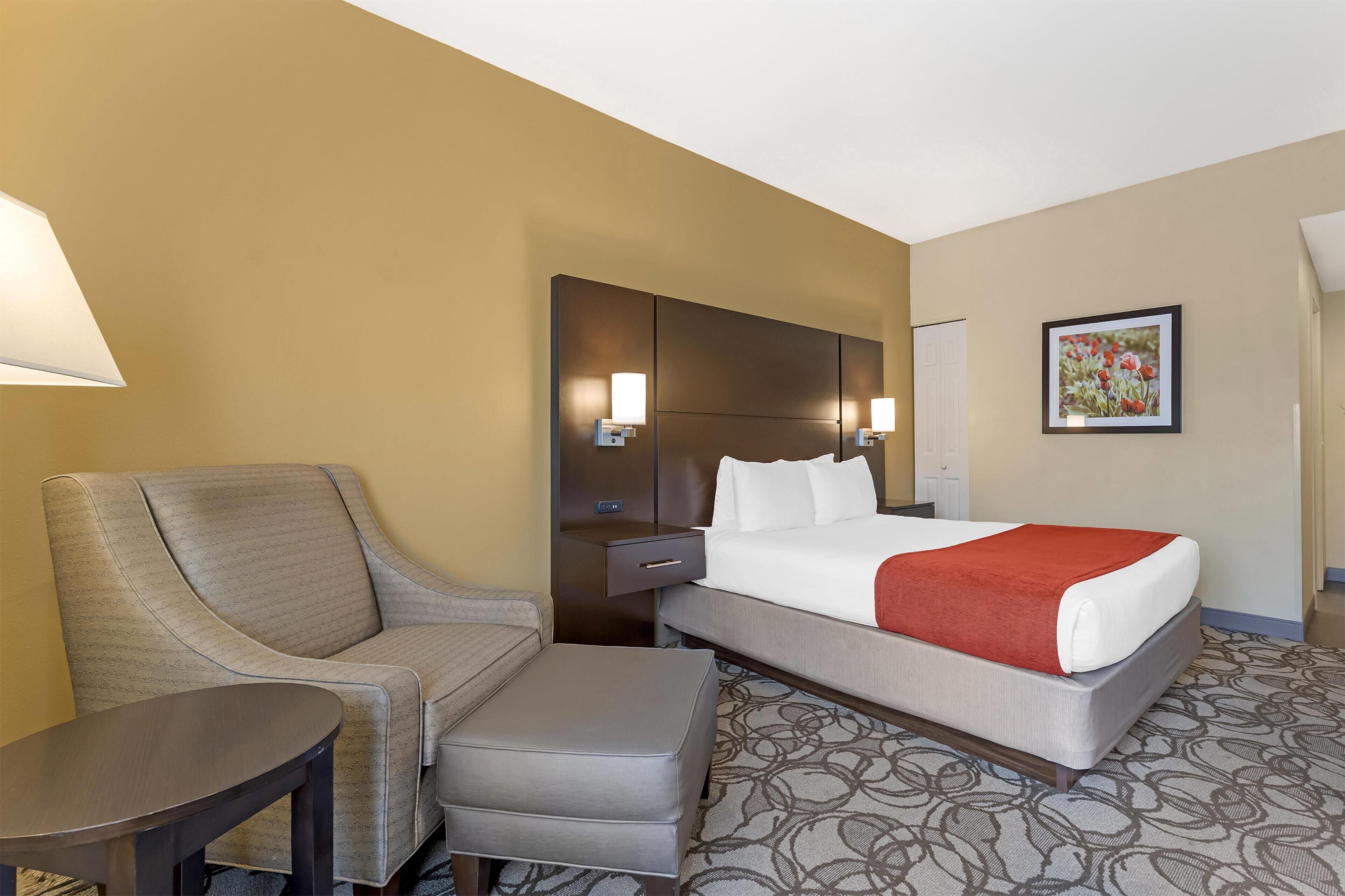 Une chambre d’hôtel comprenant un lit, un canapé, une petite table, une table de chevet et une lampe fixée au mur.