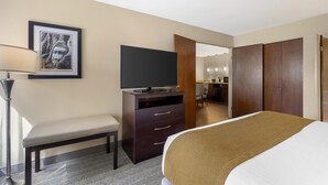 A hotel room with a bed, a desk with a TV, a bench, a framed picture on the wall, and a wardrobe. - Best Western Plus Plaza by the Green (Kent)