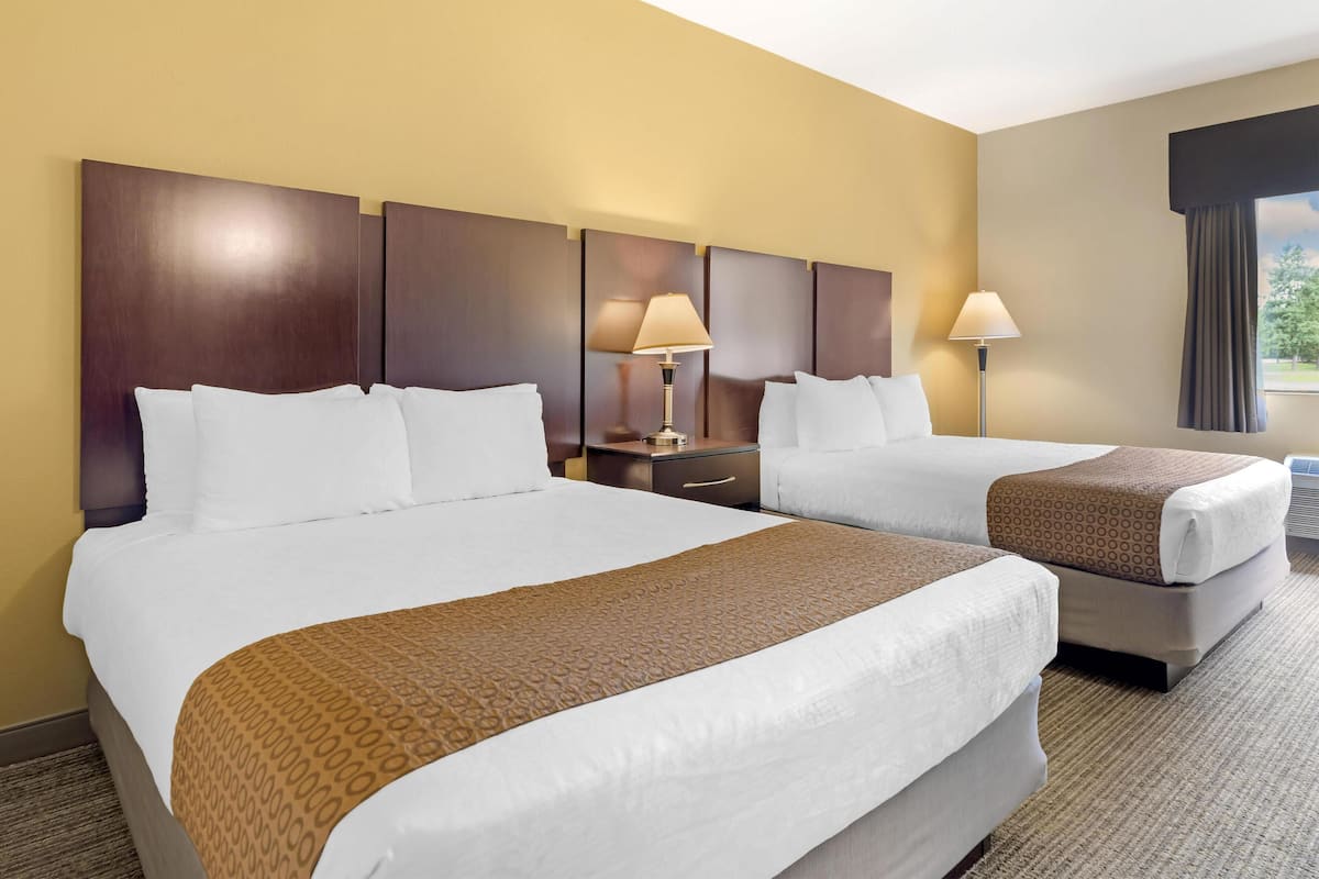 A hotel room with two beds, a nightstand, lamps, and a window with curtains.