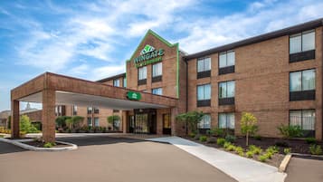 Un hotel Wingate by Wyndham con fachada de ladrillo, entrada cubierta y cielo despejado.