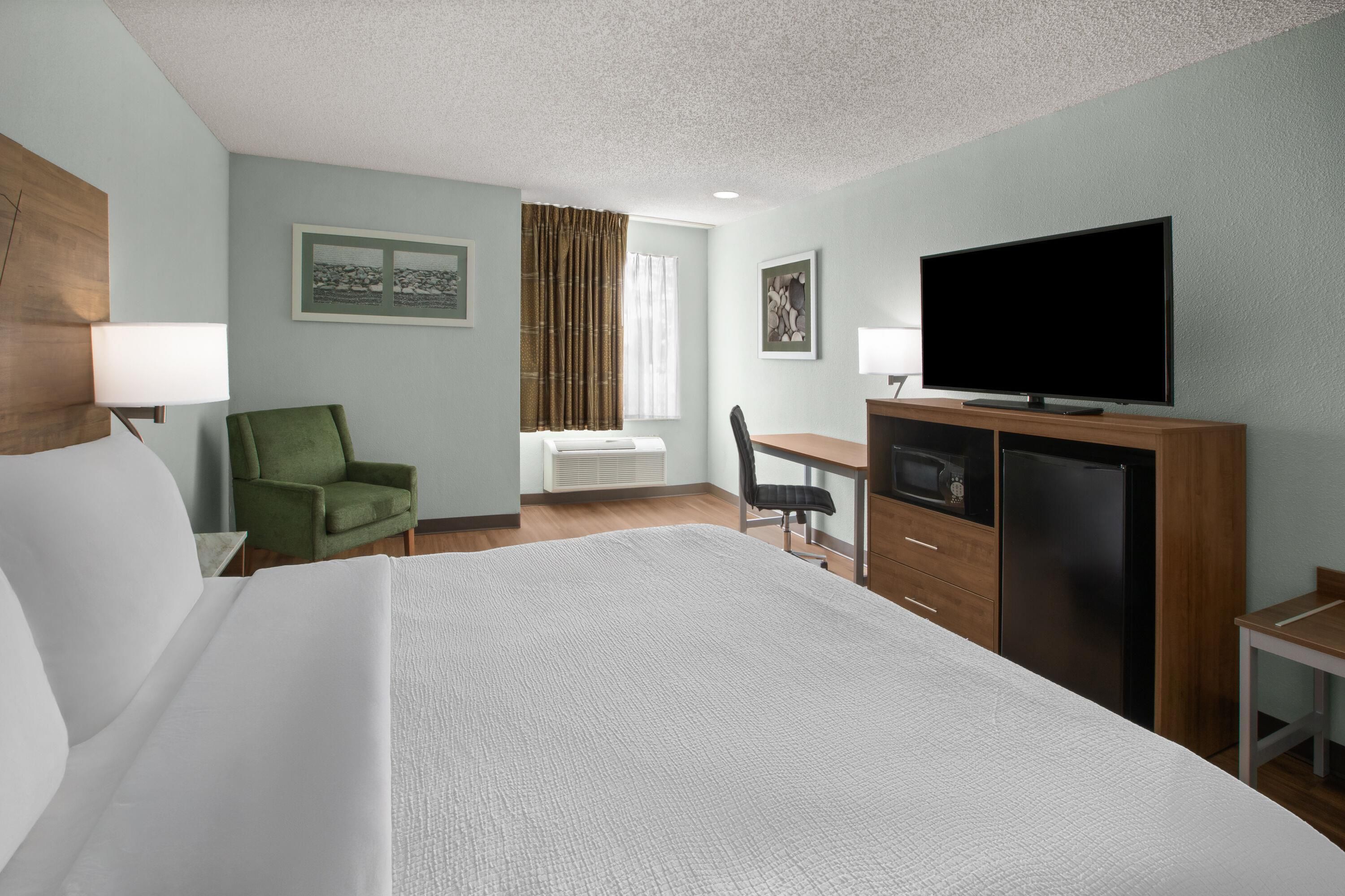 A hotel room with a bed, a desk, a television, and a chair.