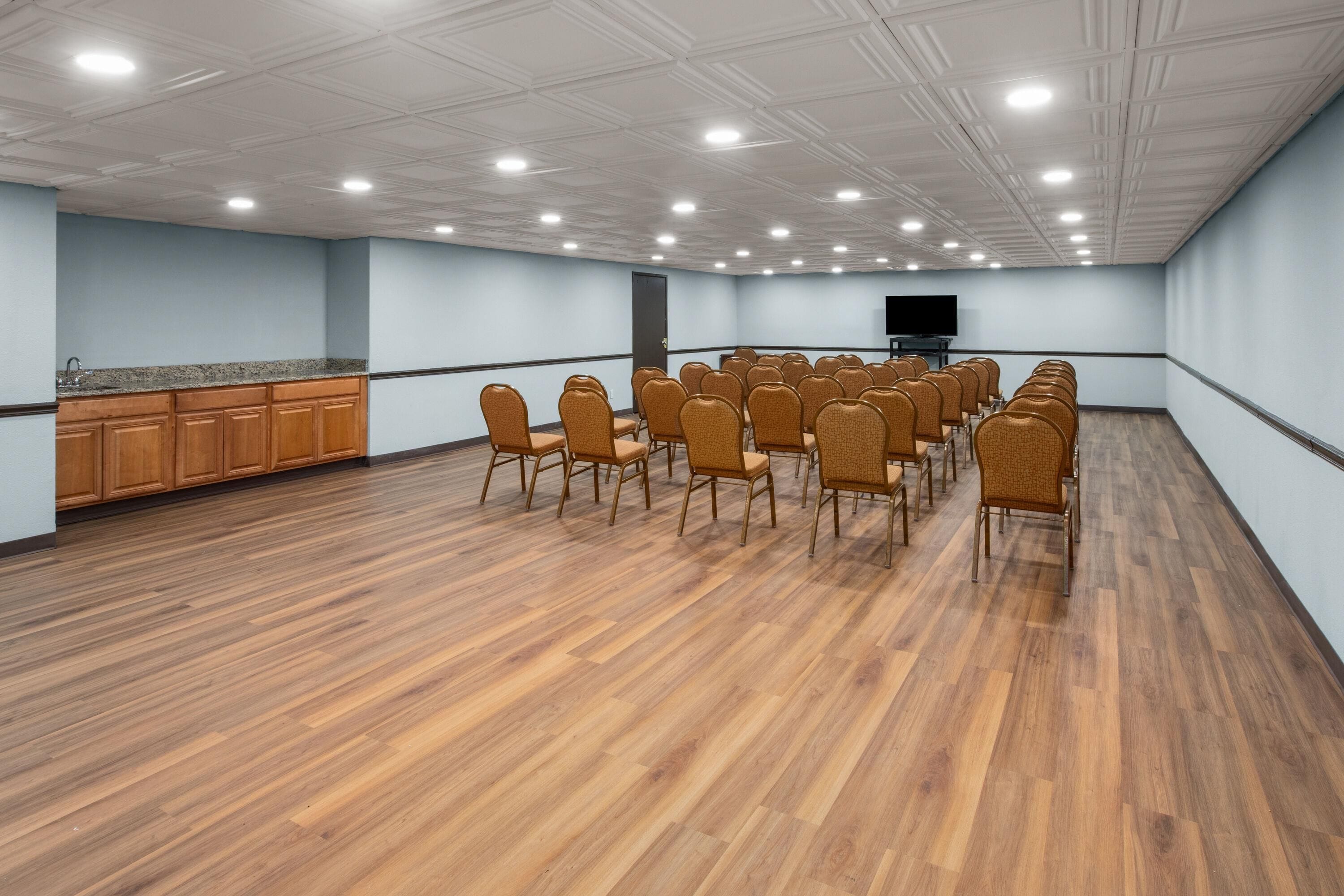 Una sala conferenze con file di sedie, un angolo cottura e una televisione a schermo piatto appesa al muro.