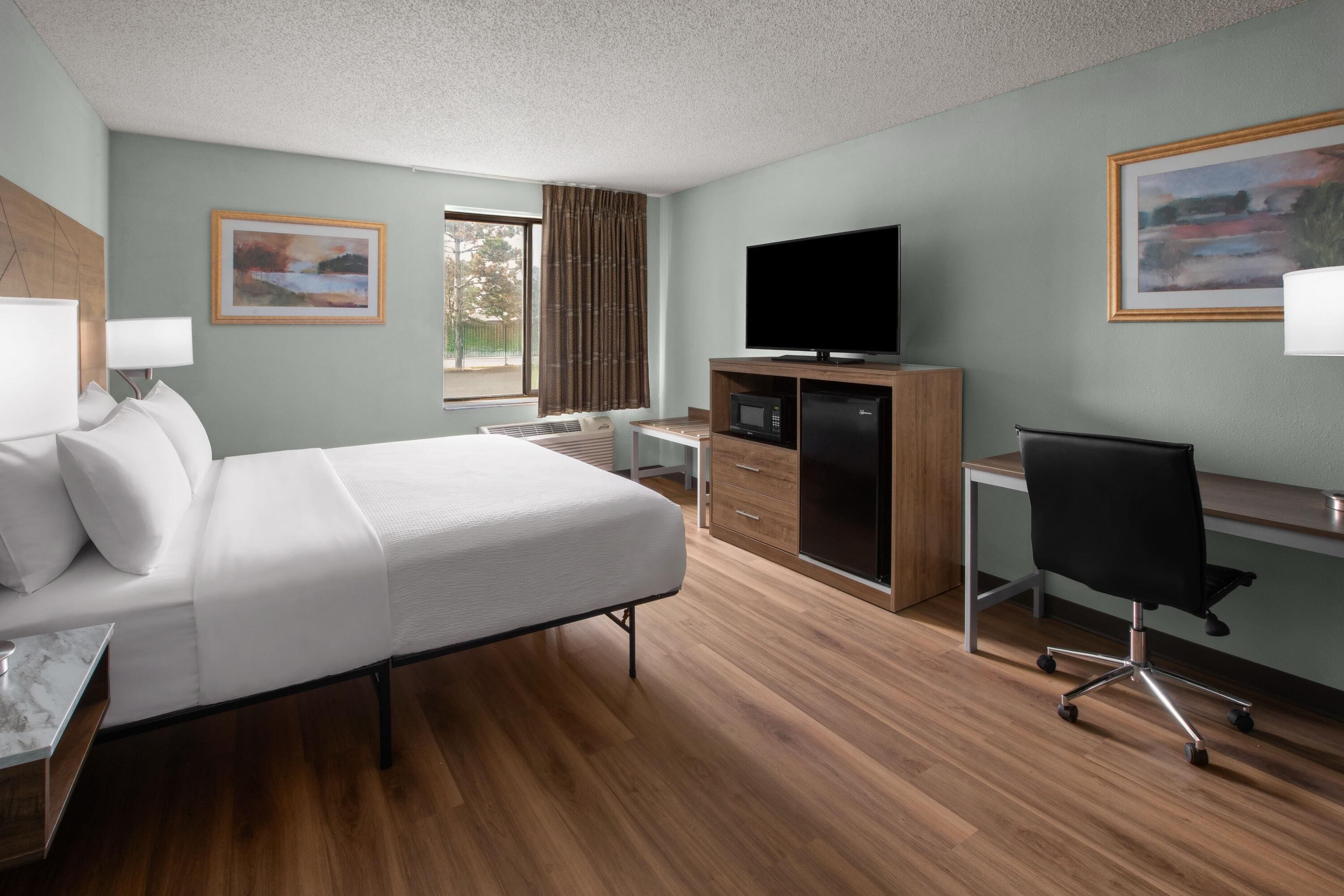 A hotel room with a bed, desk, chair, television, and artwork on the walls.