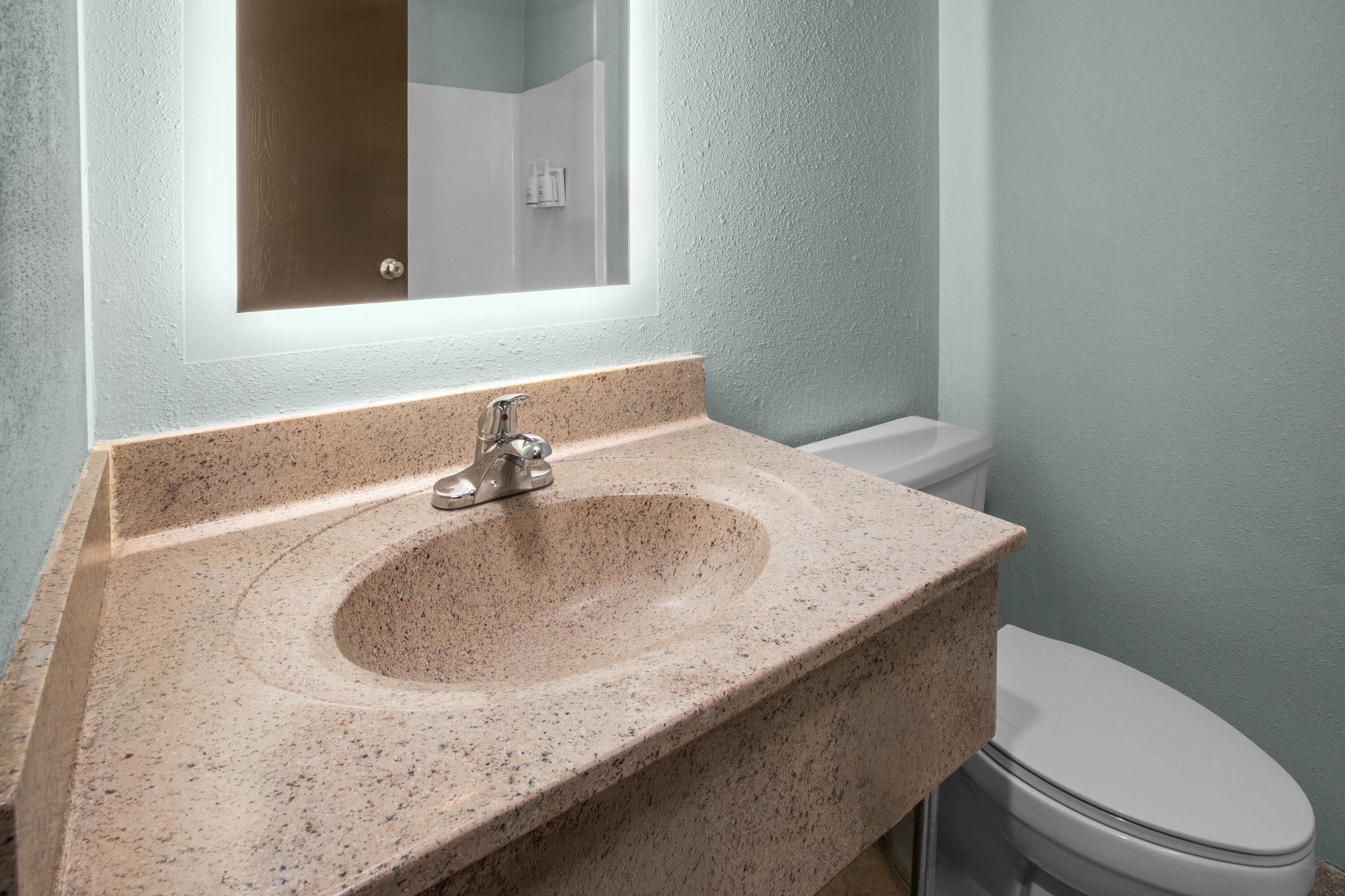 A bathroom with a granite sink, a mirror, and a toilet.