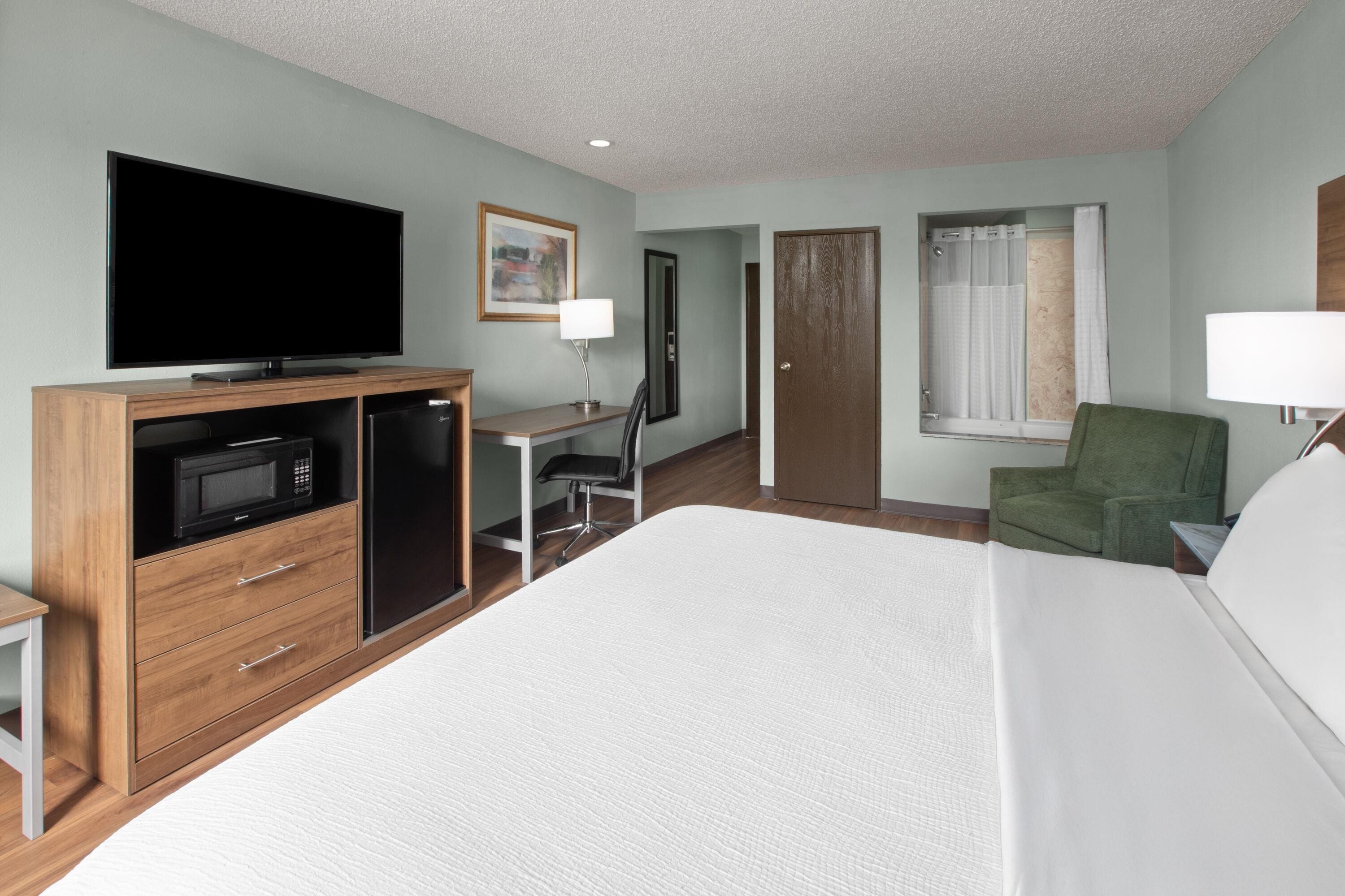 Una habitación de hotel con una cama, televisión, escritorio, silla, microondas y una puerta.
