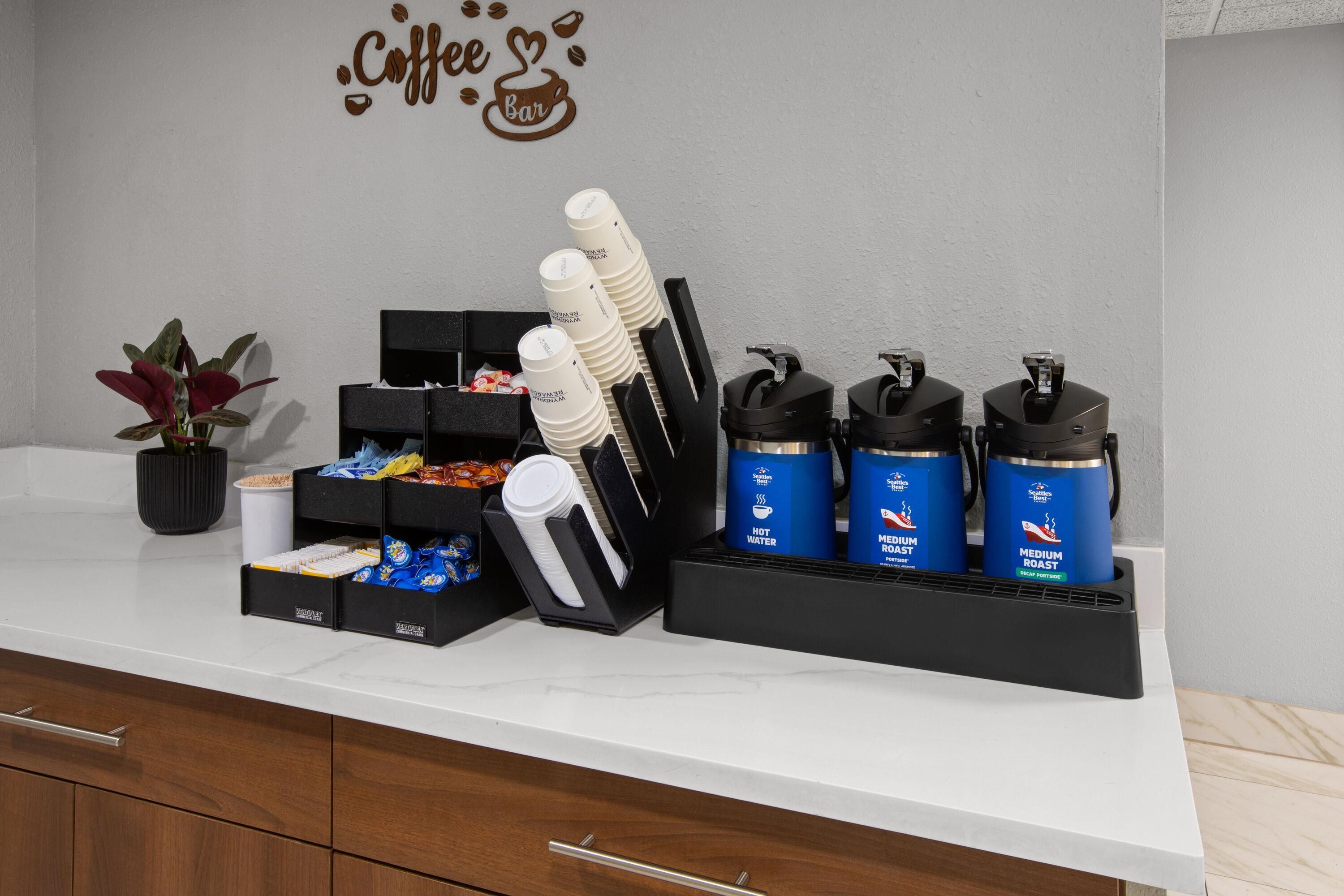 A coffee station with a coffee cup dispenser, paper cups, and a coffee machine.