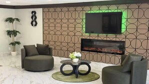 Ein modernes Wohnzimmer mit einer Couch, einem Sessel und einem runden Tisch mit Blumenvase. Ein Flachbildfernseher ist an der Wand über einem Kamin befestigt.