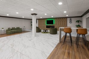A modern interior with a seating area, a dining space, and a flat-screen TV mounted on a patterned wall. - Wingate by Wyndham Livonia (Livonia)