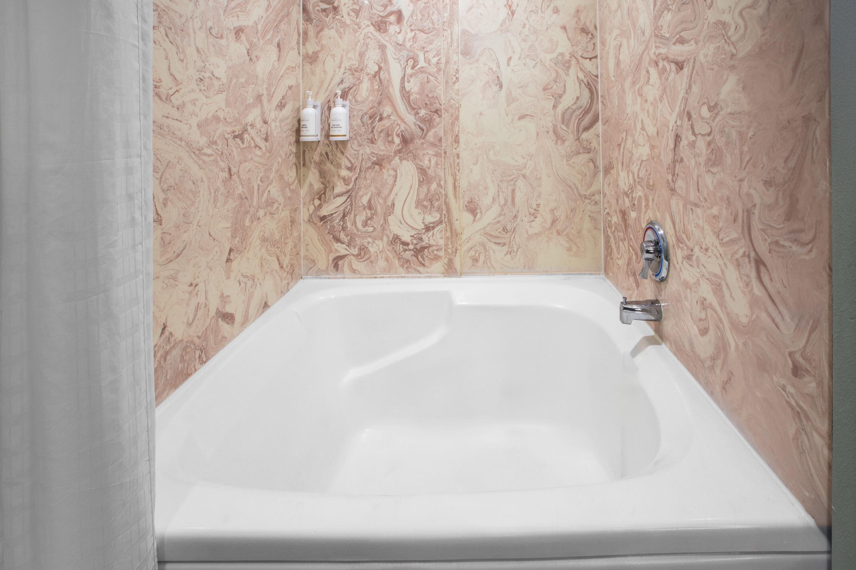 A bathroom with a white bathtub, marble-patterned walls, and a showerhead.