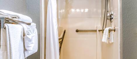 Un baño moderno con cabina de ducha de vidrio, un perchero con toallas dobladas y un pasamanos.