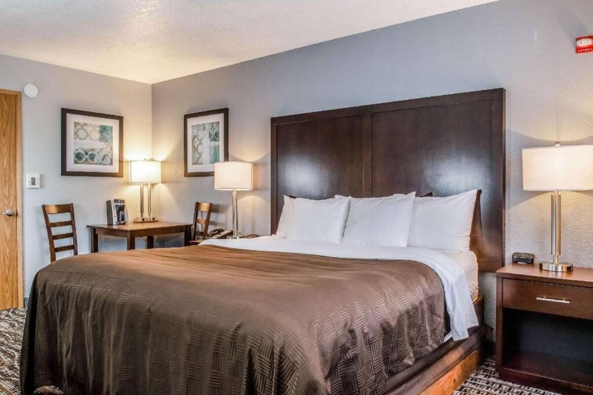 Une chambre d’hôtel avec un grand lit, deux tables de chevet, une chaise et des œuvres d’art encadrées accrochées aux murs.