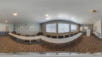 Un salón de conferencias con una mesa curva, sillas y piso alfombrado.