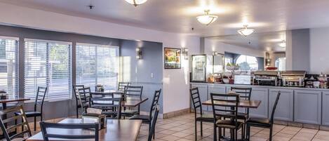 Un restaurante con mesas, sillas, una zona de cocina y amplios ventanales.