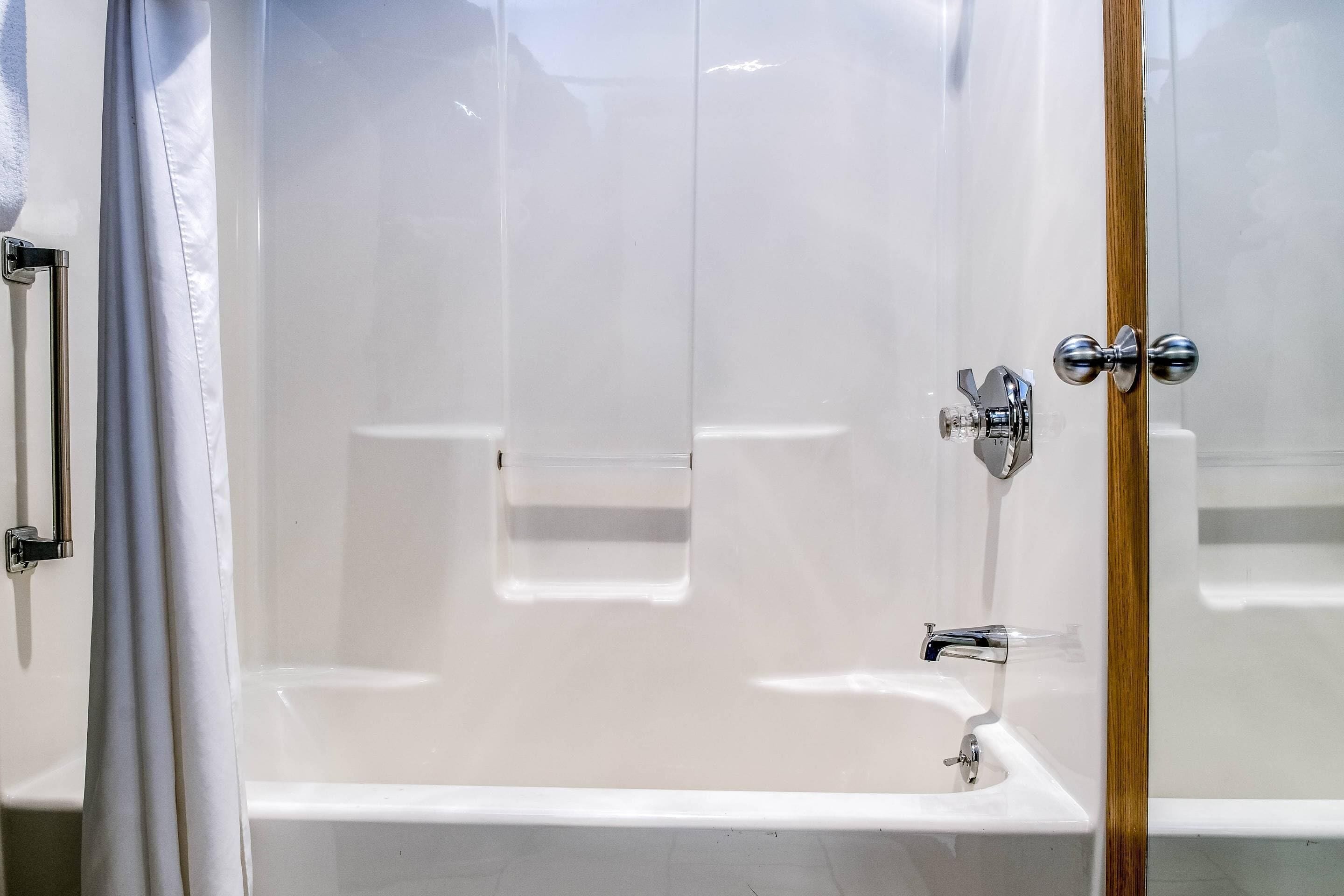 A modern bathroom with a glass shower enclosure, a white bathtub, and a wooden door.