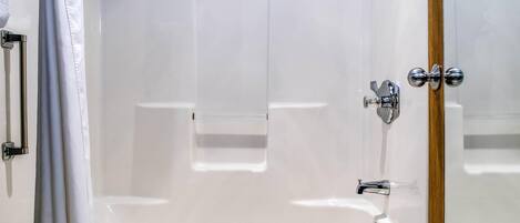 A modern bathroom with a glass shower enclosure, a white bathtub, and a wooden door.