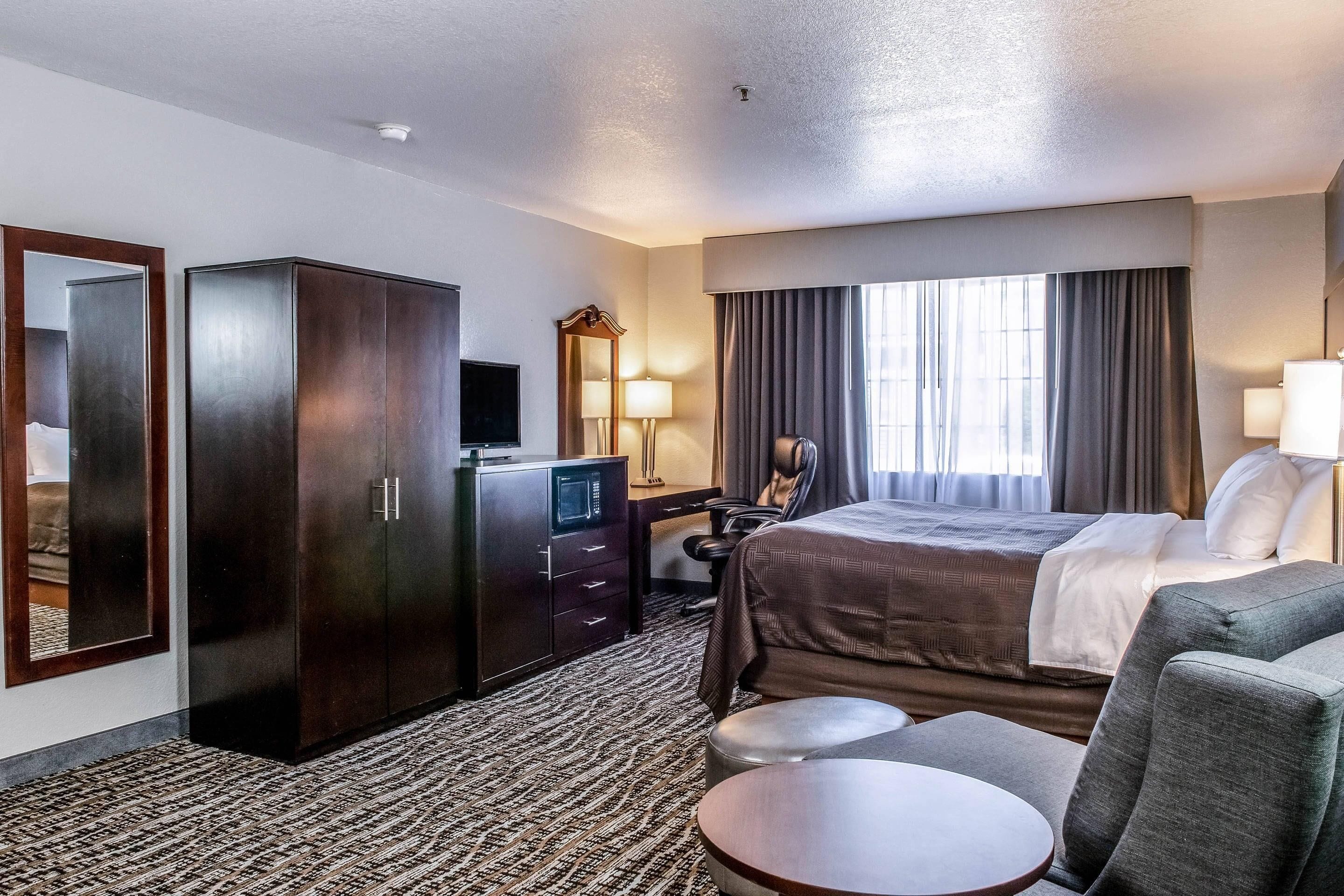 Ein Hotelzimmer mit einem Bett, einem Schreibtisch mit Computer, einem Kleiderschrank, einem Fernseher und einer Sitzecke mit Tisch und Stühlen.