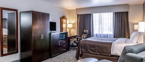 A hotel room with a bed, a desk with a computer, a wardrobe, a television, and a seating area with a table and chairs.