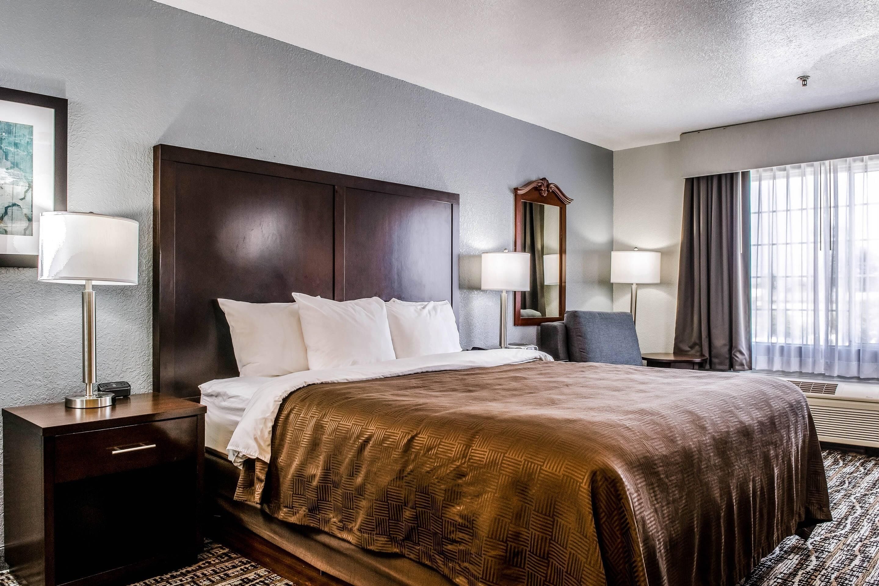 A hotel room with a large bed, two bedside tables with lamps, a mirror, and a window with curtains.