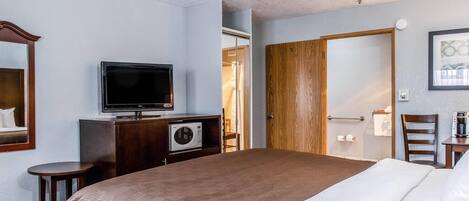 Ein Hotelzimmer mit einem großen Bett, einem Fernseher auf einer Kommode, einer Mikrowelle, einem Holzschrank und einem gerahmten Bild an der Wand.